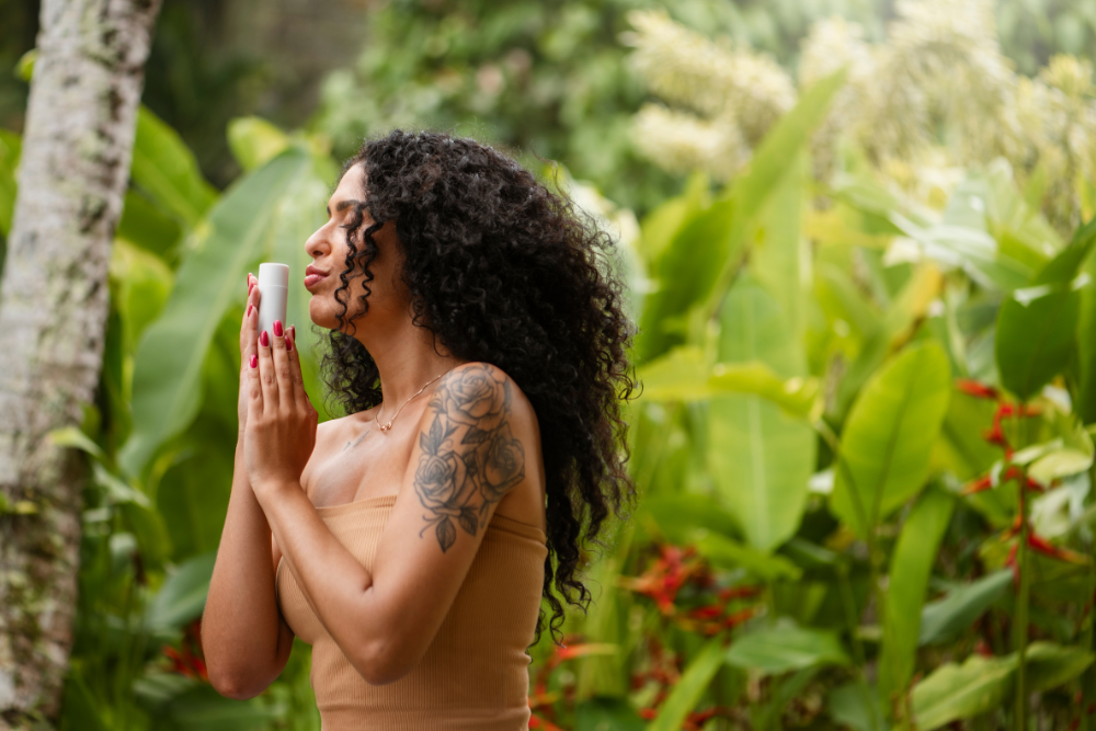 A woman with curly hair and a floral tattoo holds a ceremonial bottle close to her face, immersed in a moment of gratitude and connection with nature at an Ayahuasca retreat in Colombia.