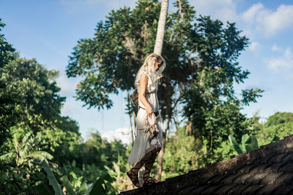 A woman in a flowing white dress walks mindfully on a rustic rooftop, surrounded by lush greenery at an Ayahuasca retreat in Colombia, embracing a spiritual and transformative journey.