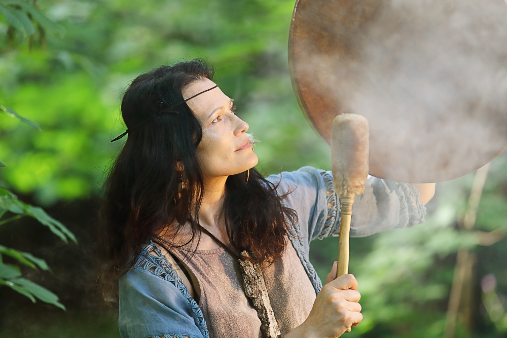Shamanic healer drumming in a forest ceremony with rising smoke, symbolizing spiritual cleansing and ayahuasca retreat rituals in Ecuador.