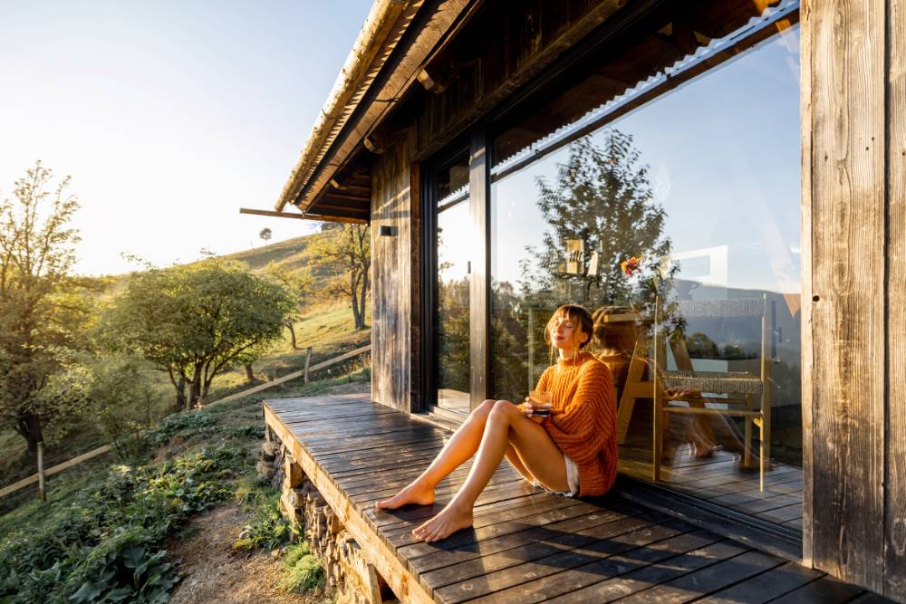 A woman enjoys a peaceful moment outside a rustic cabin in the hills during Psilocybin Retreats in Portugal, soaking in the golden sunset.