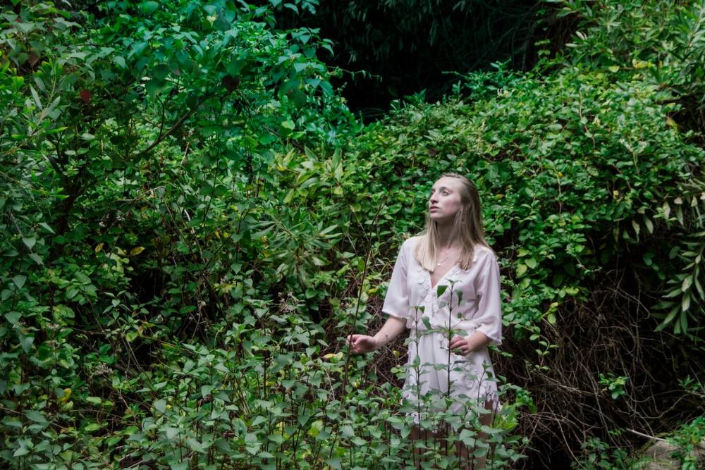 A woman wanders mindfully through lush forest surroundings, symbolizing the nature immersion experienced during Psilocybin Retreats in the USA.