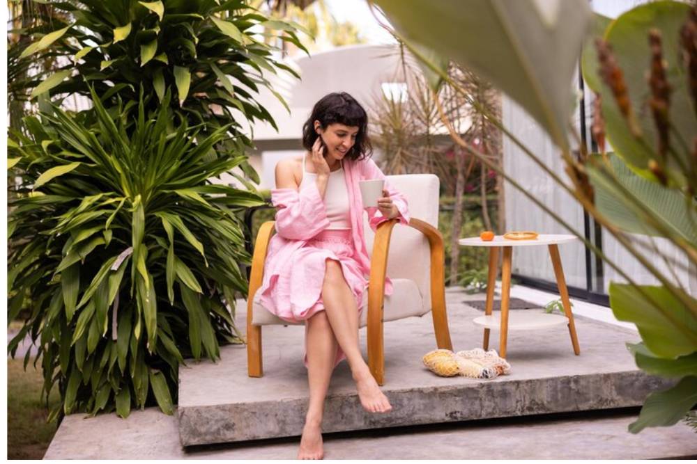 Woman in a pink robe sipping tea in a lush garden, representing the relaxation and reflection found at San Pedro retreats in Peru.