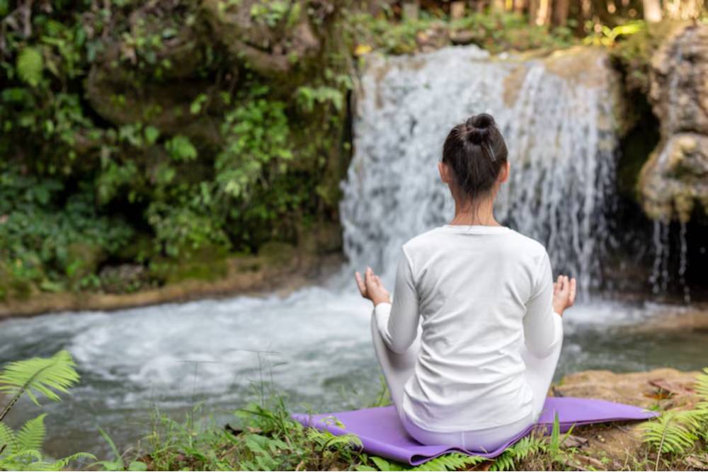 Woman meditating beside a serene waterfall, immersed in the healing nature of San Pedro Retreats in Ecuador.
