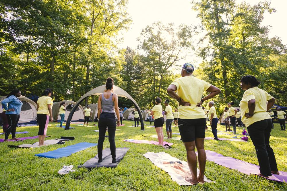 A large group practices outdoor movement exercises in a forested retreat space with tents, part of a community healing event during Iboga Retreats in Costa Rica.