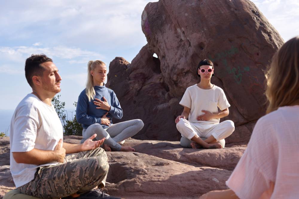A small group of people sit in meditation on rocks during a healing session at one of the Iboga Retreats in Costa Rica, surrounded by natural stone formations.