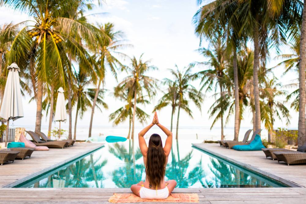 A woman practicing yoga at a serene beachfront pool lined with palm trees during her Iboga Retreat in Mexico.