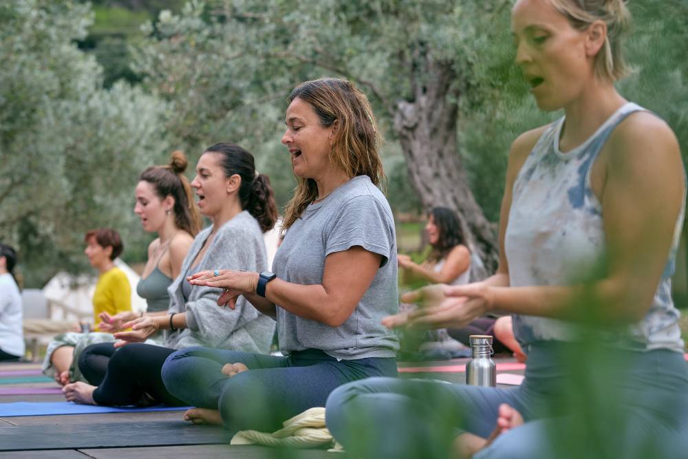 A group of women participating in a healing session at Iboga Retreats in Mexico, seated in meditation and chanting surrounded by nature.