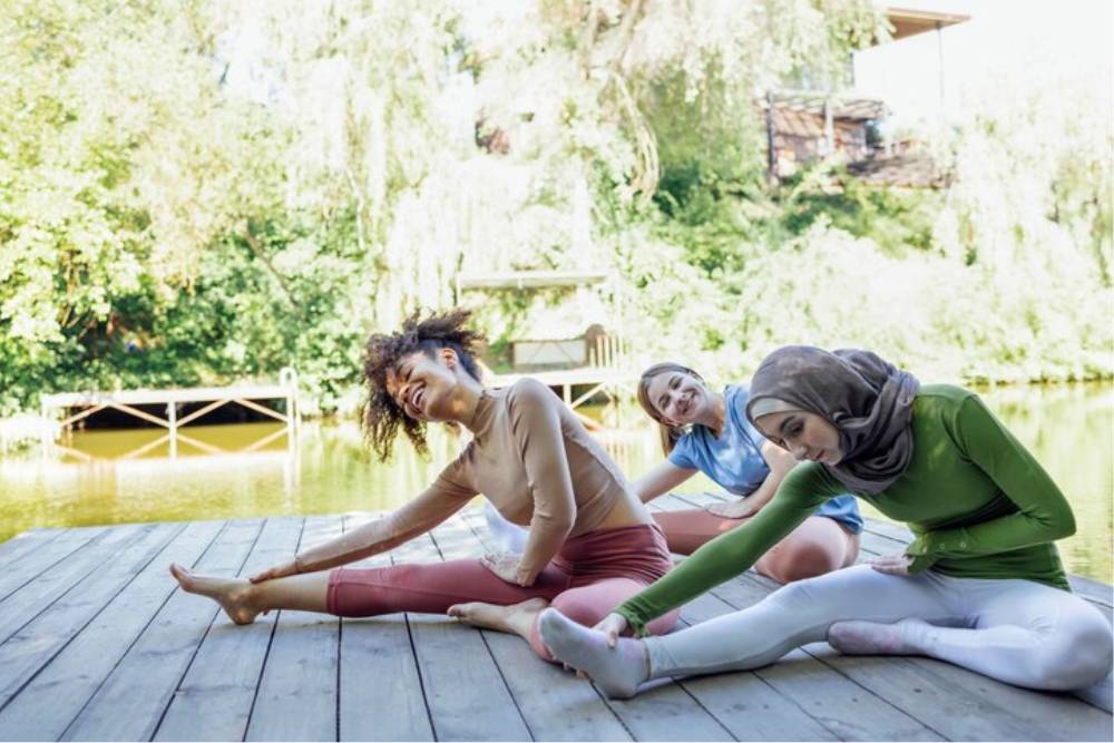 A diverse group of women stretching by a serene lakeside, participating in wellness activities at Iboga Retreats in Canada.