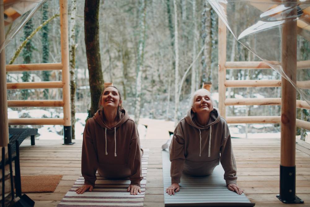 Women practicing yoga on a forest cabin deck surrounded by snowy trees, enjoying rejuvenation at Iboga Retreats in Canada.
