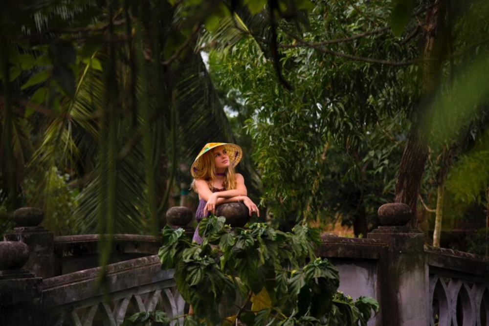 A reflective woman in a straw hat leans on a stone bridge surrounded by tropical greenery, capturing the introspective journey at Psilocybin Retreats in Costa Rica.