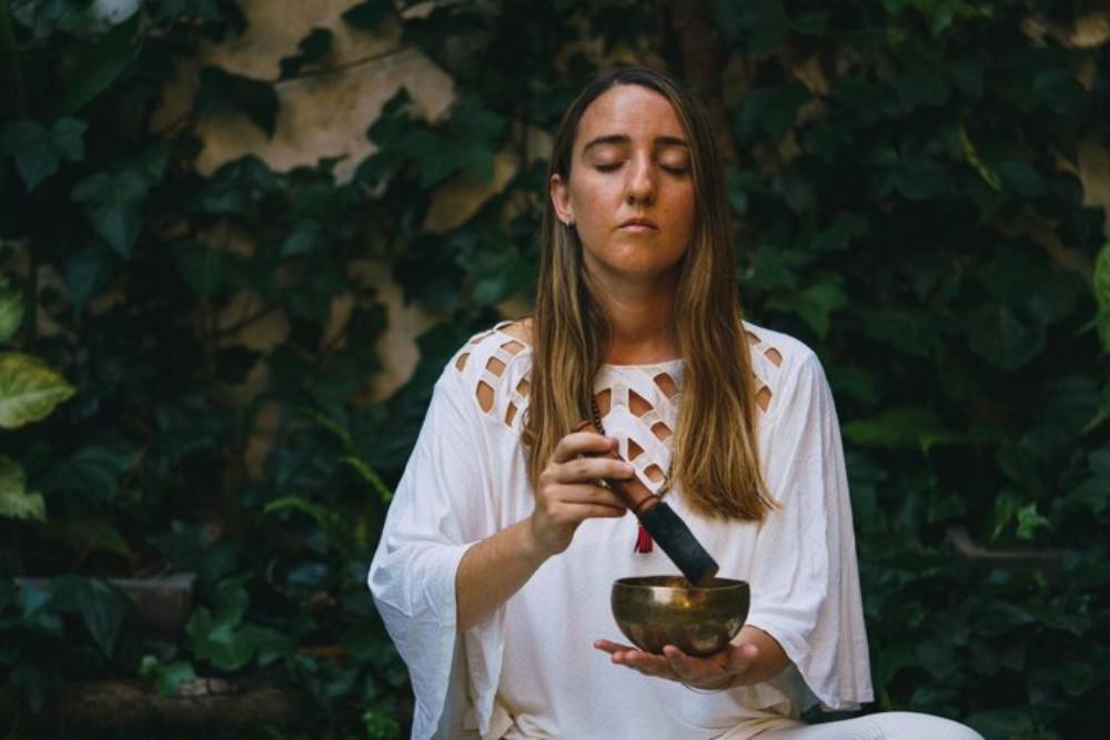 Woman meditating with a sound bowl in nature, reflecting on what does the San Pedro cactus do to enhance meditative and emotional states.