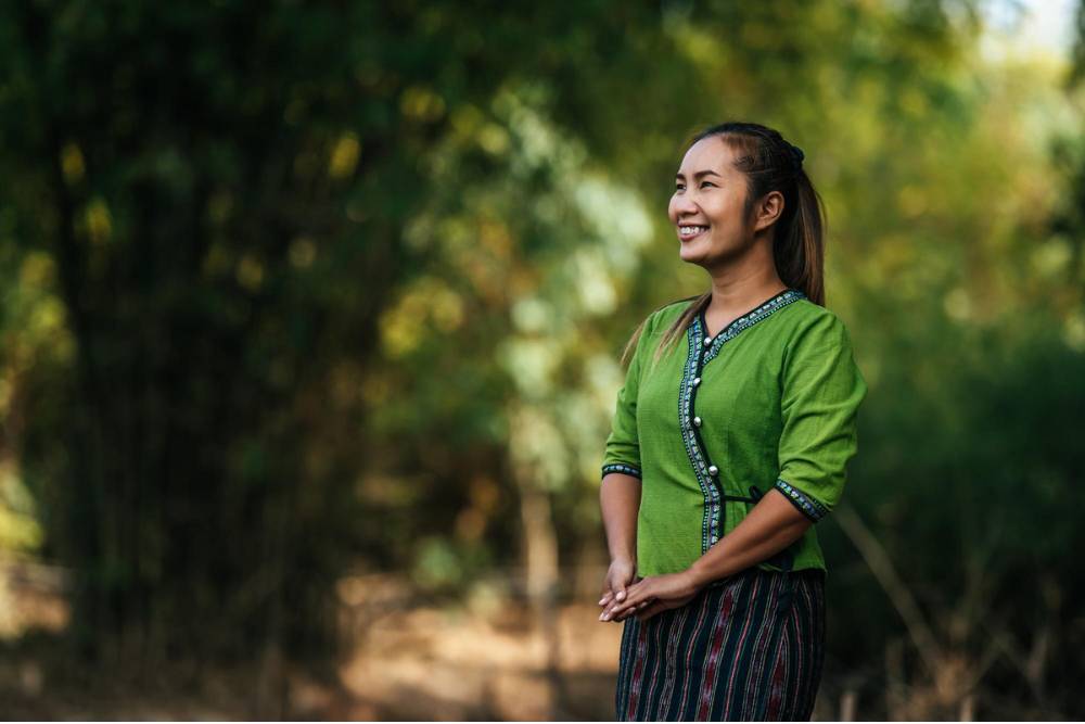 A smiling woman stands amidst lush greenery, radiating calm and joy during Peyote Retreats in Peru.